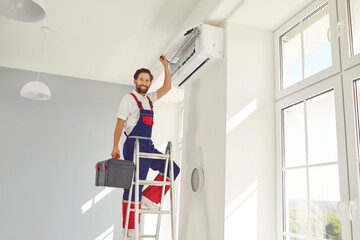 Portrait of professional electrician man or technician with toolbox standing on ladder,looking at...