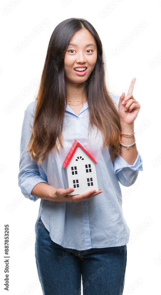 Poster Young asian woman real state agent holding house isolated background surprised with an idea or question pointing finger with happy face, number one