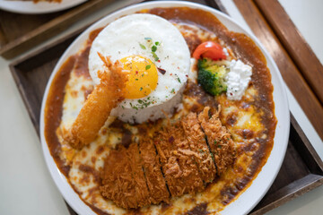 a plate of food with a fried pork cutlet, white rice topped with a fried egg, and a side of broccoli and tomato