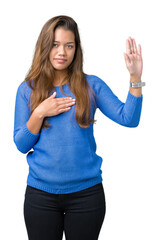 Young beautiful brunette woman wearing blue sweater over isolated background Swearing with hand on...