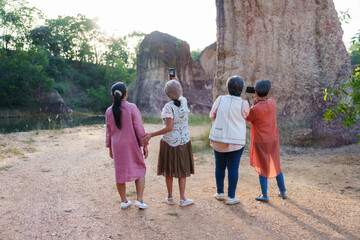 Group of elderly Asian women enjoying an outdoor hike, exploring a rocky area. Casual attire, holding water bottles, sunny day, sharing laughter and conversation, surrounded by nature,