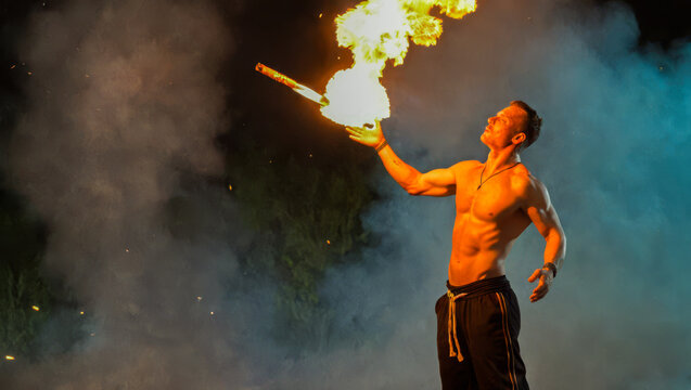 Fire breather in action, night time spectacle, artist skillfully controlling flames, captivating outdoor entertainment, bright fire against dark backdrop, solo performer in dramatic show