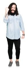 Obraz premium Young hipster man with long hair and beard wearing glasses angry and mad raising fist frustrated and furious while shouting with anger. Rage and aggressive concept.