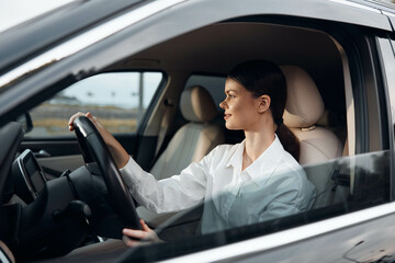 Naklejka premium Woman, driver, car interior a woman with a confident expression sits in the driver's seat of a car, her hand resting on the steering wheel while she looks directly at the camera