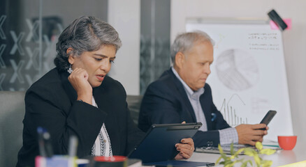 Indian old aged adult gen x woman lady use tablet look screen talk distant office place older elder boss ceo man agent expert male hold mobile phone read news check email data do job work spend time