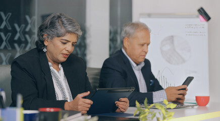 Indian old aged adult gen x woman lady use tablet look screen talk distant office place older elder boss ceo man agent expert male hold mobile phone read news check email data do job work spend time