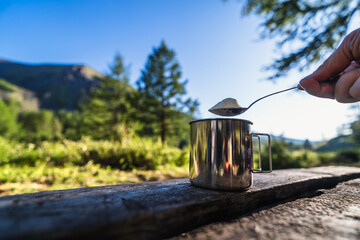 Adding a spoonful of powdered milk to morning coffee at the campsite
