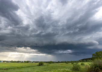 An ominous yet beautiful springtime sky hangs over a peaceful meadow, with a few trees silhouetted in the distance.