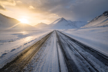 Straight road in southern Iceland at sunset, in winter, icy slippery road with mountains visible