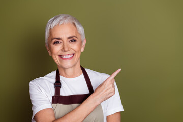 Photo of charming positive woman wear apron serving coffee pointing empty space isolated khaki color background