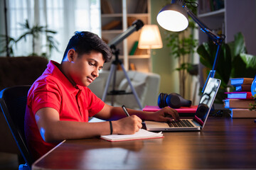ndian Asian teenage student learning online with computer, headphones, and smartphone