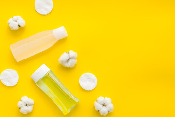 facial tonic, lotion and cotton pads for face care on yellow background top view mock up
