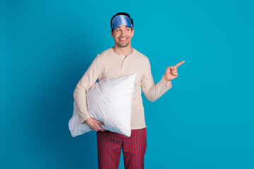 Portrait of nice young man cushion indicate finger empty space wear pajama isolated on blue color background