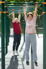 Obraz premium Elderly man and woman doing exercises in sports bars on outdoor sports ground