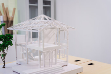 Desk of an engineer displays a concrete house structure under construction. A toy house model sits...