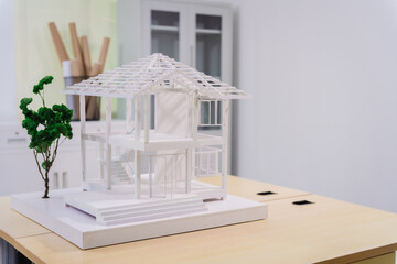 Desk of an engineer displays a concrete house structure under construction. A toy house model sits...