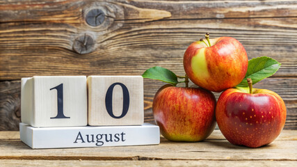 Wooden calendar displaying August 10 next to a stack of fresh red apples with green leaves, set against a rustic wooden background.