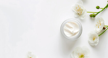 Glass jar with face cream on a white background, decorated with flowers. Top view. Copy space. Mockup