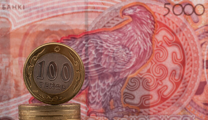 A coin of 100 Kazakhstan tenge against the background of a new 5000 tenge banknote
