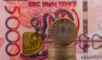 A coin of 100 Kazakhstan tenge against the background of a new 5000 tenge banknote