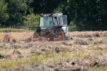 Fototapeta premium Raking and Baling Hay in summer with tractor and attachments