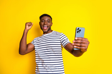 Photo of nice young man smart phone raise fist wear striped t-shirt isolated on bright yellow color background