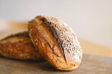 Two loaves of sourdough bread, freshly baked and still warm, are stacked on a wooden surface. The...