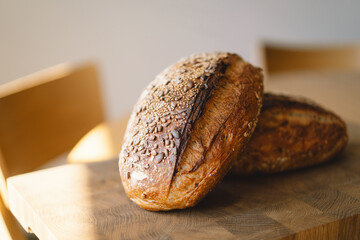 Two loaves of sourdough bread, freshly baked and still warm, are stacked on a wooden surface. The...