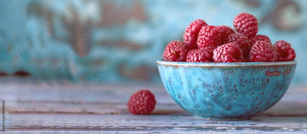 Aufkleber fresh raspberries placed in a blue ceramic bowl on a walnut table with a blurred background for copy