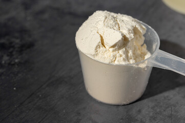 Heap of protein powder in a scoop. Food supplements. Dark background. Bodybuilding, fitness, gym.