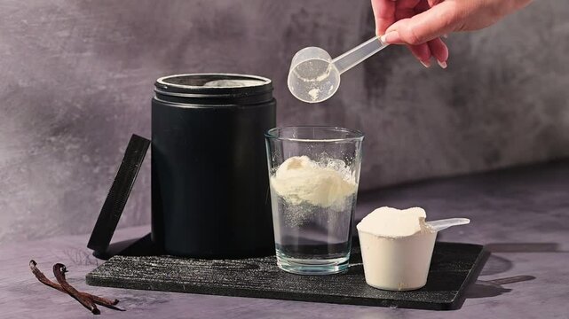 Protein powder. Pouring whey, vanilla protein powder, in a glass. Food supplements. Dark background. Bodybuilding, fitness, gym.