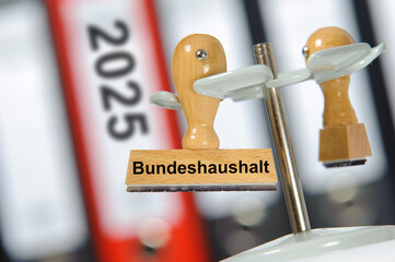 Ein Holzstempel ist beschriftet mit dem Aufdruck: Bundeshaushalt 2025