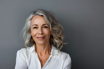 studio portrait of stylish middle age smiling 50 - 55 year old woman posing on grey background