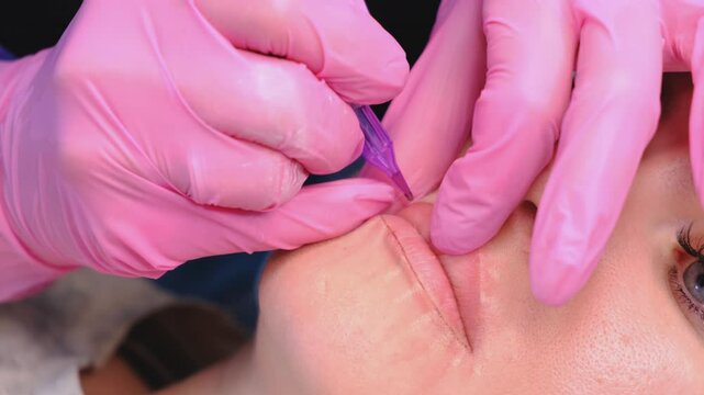 Procedure permanent makeup in beauty salon, tattoo machine with red pigment on woman lips.