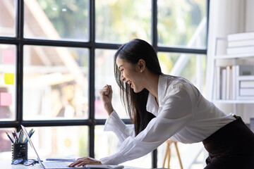 Successful Asian businesswoman happy looking at laptop and excited. Woman in office looking at laptop surprised to receive bonus and promotion.