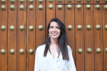 young and beautiful latin woman looks at different places in the street, the woman has a wooden...