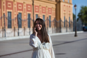 Fototapeta premium Young and beautiful Latin woman talking on mobile phone is having fun and is happy and smiling loudly. The woman is on the street and walks through the city. Concept communications.
