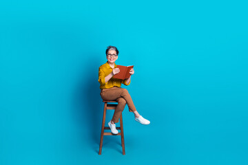 Full length photo of charming positive woman wear blue blouse eyeglasses sitting chair enjoy book...