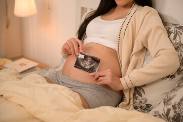 Pregnant woman holding ultrasound picture in bedroom