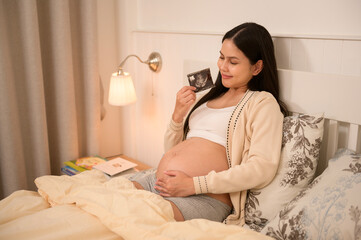 Pregnant woman holding ultrasound picture in bedroom
