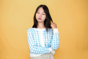 young asian woman playing or holding her hair isolated on yellow background