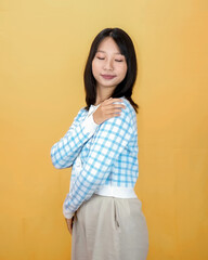 Happy mindful thankful young woman holding hands on chest smiling isolated on yellow background feeling no stress, gratitude, mental health balance, peace of mind concept.