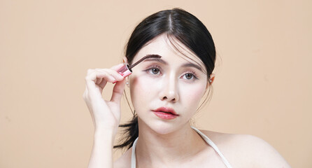 Beautiful Asian woman holding mascara brush uses eyelashes to make beautiful eyes in studio
