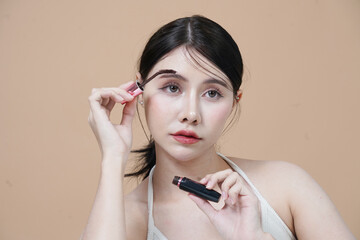 Beautiful Asian woman holding mascara brush uses eyelashes to make beautiful eyes in studio
