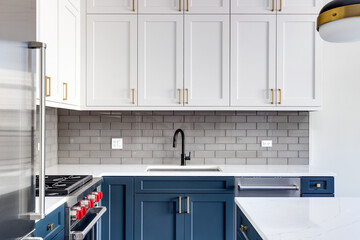 Detail shot of a kitchen with blue and white cabinets, black faucet, and a subway tile backsplash.