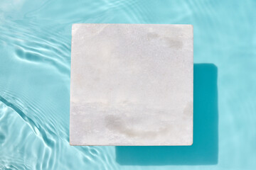Podium for cosmetic presentation. A marble tile submerged in a clear blue pool with water ripples...