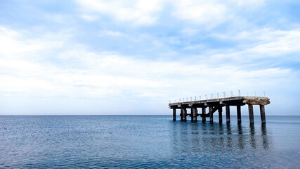 Fototapeta premium Destroyed pier in Batumi, Georgia. Damaged concrete construction in the Black sea. Calm weather, cloudy skies in the background