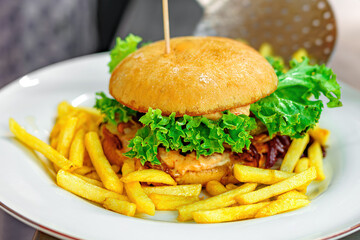 A cook in a restaurant prepares a bacon burger and cutlets with salad and cheese.