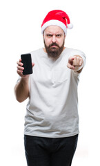 Young caucasian man wearing christmas hat showing smartphone screen over isolated background pointing with finger to the camera and to you, hand sign, positive and confident gesture from the front