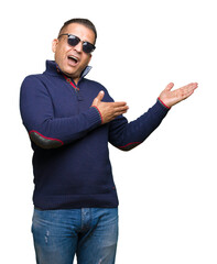 Fototapeta premium Middle age arab man wearing sunglasses over isolated background amazed and smiling to the camera while presenting with hand and pointing with finger.